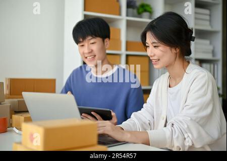 Une belle jeune femme asiatique propriétaire de boutique en ligne parle et vérifie le stock de produits sur l'ordinateur avec son petit ami dans le bureau à domicile. Banque D'Images