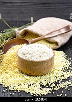 Flocons de millet dans un bol, gémissement dans une cuillère, sur une table et dans un sac de toile de jute, tiges avec des épis de millet sur le fond de bois Banque D'Images