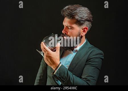 Homme barbu en costume noir et verre de whisky en loft. Homme plein de confiance et bien habillé avec un verre de whisky. Banque D'Images