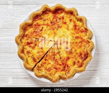 quiche de petit déjeuner moelleuse avec garniture au fromage et au bacon sur une assiette blanche sur une table en bois blanc, vue horizontale depuis le dessus, plat, gros plan Banque D'Images