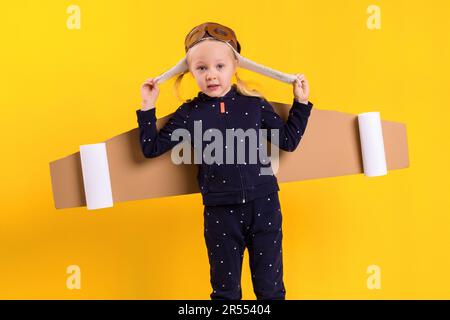 Une petite fille porte des ailes volantes en carton faites maison, prétendant être un pilote pour un concept d'artisanat, d'imagination ou d'exploration. Banque D'Images