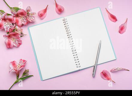 Le carnet est entouré de fleurs et de pétales roses Alstroemeria sur fond rose Banque D'Images