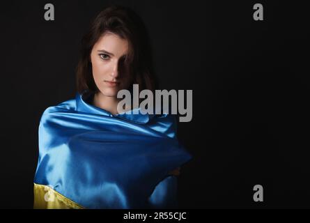 Triste femme enveloppée dans le drapeau ukrainien sur fond noir. Espace pour le texte Banque D'Images