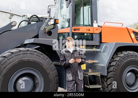 Technicien de maintenance équipé d'une tablette numérique sur un arrière-plan du tracteur. Photo de haute qualité Banque D'Images
