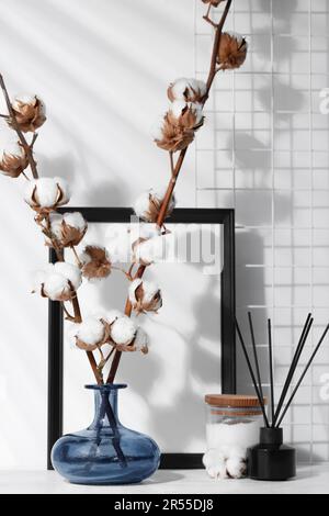 Diffuseur en roseau, bougie et branches en coton avec fleurs moelleuses sur table en bois blanc à l'intérieur Banque D'Images