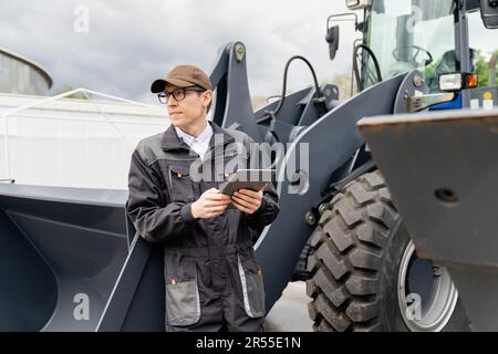 Technicien de maintenance équipé d'une tablette numérique sur un arrière-plan du tracteur. Photo de haute qualité Banque D'Images