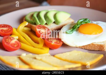 Toasts savoureux avec œuf frit, avocat, fromage et légumes sur l'assiette, en gros plan Banque D'Images