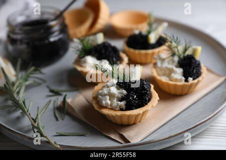 Tartelettes délicieuses avec caviar noir, fromage à la crème et citron servies sur une table en bois blanc, en gros plan Banque D'Images