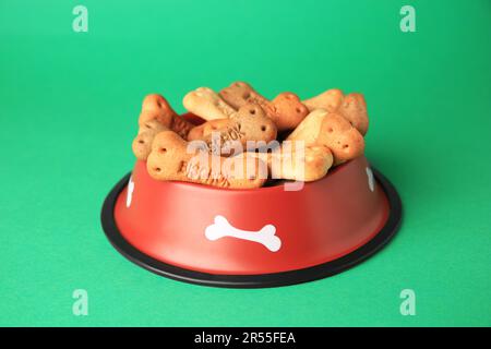 Biscuits pour chiens en forme d'os dans un bol sur fond vert Banque D'Images