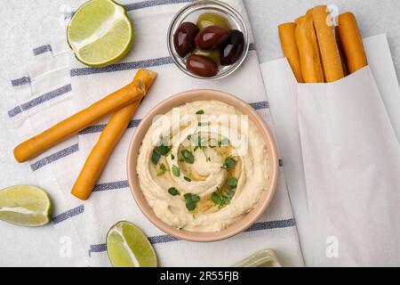 Délicieux houmous avec bâtonnets de graissini, citron vert et olives sur table gris clair, plat Banque D'Images