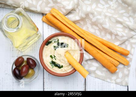 Délicieux houmous avec bâtonnets de grissini et olives sur table en bois blanc, plat Banque D'Images