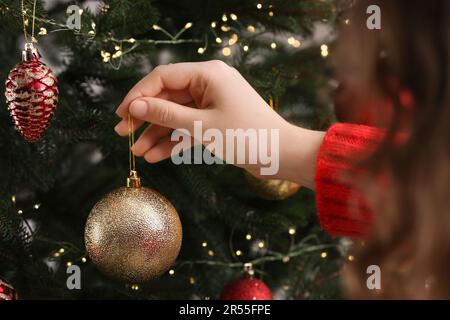 Femme décorant arbre de Noël avec belle boule, gros plan Banque D'Images