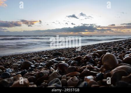 Angle bas sur Worthing Beach au coucher du soleil en janvier, montrant des galets mouillés pendant que la mer s'enrôle. Banque D'Images