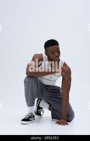 Pantalon et débardeur de jeune afro-américain musclé avec collier doré, qui pose avec assurance dans une tenue élégante et tendance Banque D'Images