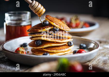 Crêpes américaines aux myrtilles, fraises et cerises avec trempette de miel. Placé sur une assiette de designer rustique, sur une planche rustique en bois. Banque D'Images