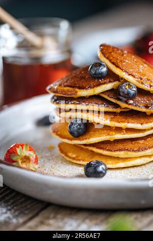 Crêpes américaines aux myrtilles, fraises et cerises avec trempette de miel. Placé sur une assiette de designer rustique, sur une planche rustique en bois. Banque D'Images
