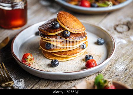 Crêpes américaines aux myrtilles, fraises et cerises avec trempette de miel. Placé sur une assiette de designer rustique, sur une planche rustique en bois. Banque D'Images