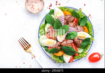 Salade Périgord avec foie de poulet rôti, tomates rouges, concombres, œufs durs, laitue et épinards. Arrière-plan de la table de cuisine noire, vue du dessus Banque D'Images