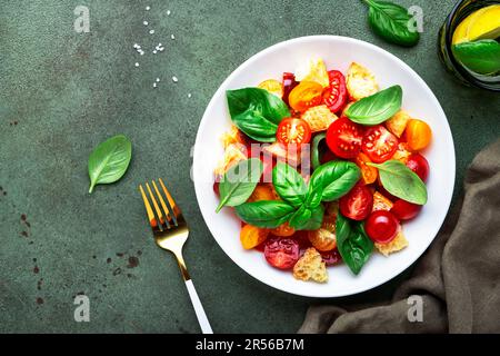 Salade de légumes d'été panzanella avec pain rassis, tomates colorées, huile d'olive, sel et basilic vert, fond de table vert, vue du dessus Banque D'Images