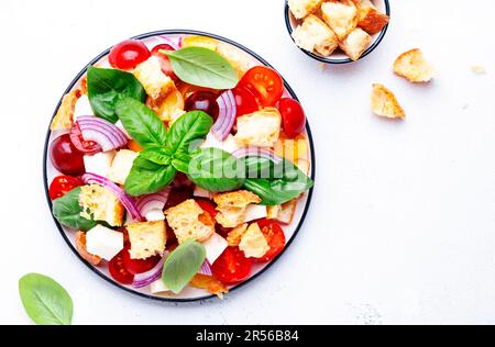 Panzanella salade de légumes italiens avec pain rassis, tomates colorées, fromage mozzarella, oignon, huile d'olive, sel et basilic vert, fond de table blanc Banque D'Images