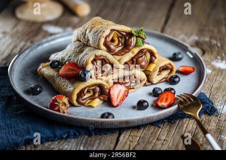 Crêpes avec garniture au chocolat disposées en forme de pyramide avec des fraises de saison, des cerises et des myrtilles sur une assiette bleue rustique Banque D'Images