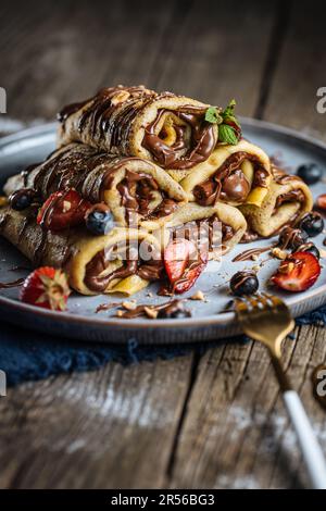 Crêpes avec garniture au chocolat disposées en forme de pyramide avec des fraises de saison, des cerises et des myrtilles sur une assiette bleue rustique Banque D'Images
