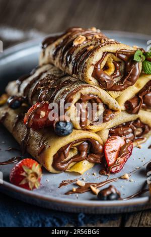 Crêpes avec garniture au chocolat disposées en forme de pyramide avec des fraises de saison, des cerises et des myrtilles sur une assiette bleue rustique Banque D'Images