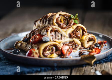 Crêpes avec garniture au chocolat disposées en forme de pyramide avec des fraises de saison, des cerises et des myrtilles sur une assiette bleue rustique Banque D'Images