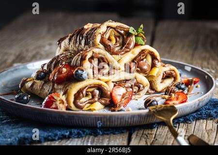 Crêpes avec garniture au chocolat disposées en forme de pyramide avec des fraises de saison, des cerises et des myrtilles sur une assiette bleue rustique Banque D'Images