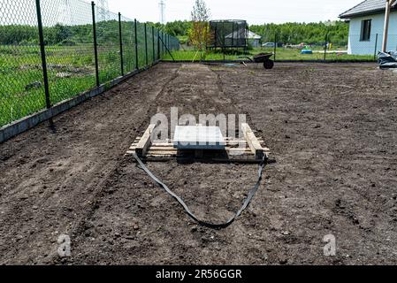 Nivellement du chernozem dans la cour avec une palette pondérée avec un cube en béton, en préparation pour semer la pelouse. Banque D'Images