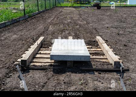 Nivellement du chernozem dans la cour avec une palette pondérée avec un cube en béton, en préparation pour semer la pelouse. Banque D'Images