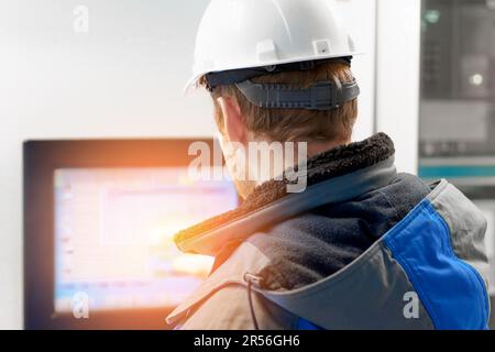 Un ingénieur dans un casque blanc pointe vers l'écran tactile du système de commande automatique au gaz naturel. Équipement numérique moderne dans l'industrie du gaz. Vue arrière. Flux de travail authentique. Banque D'Images