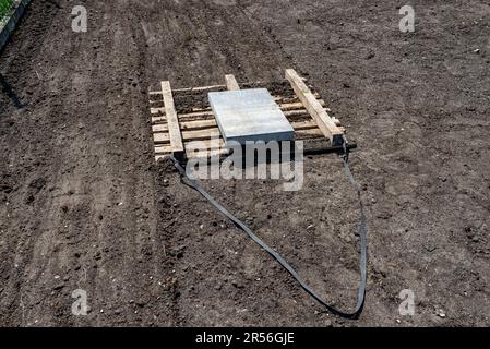 Nivellement du chernozem dans la cour avec une palette pondérée avec un cube en béton, en préparation pour semer la pelouse. Banque D'Images