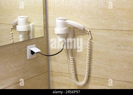 Sèche-cheveux blanc sur carrelage en céramique beige dans la salle de bains de l'hôtel. Concept de service d'hébergement de l'hôtel Banque D'Images