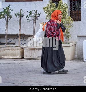 Mahdia, Tunisie, 29 janvier 2023: Une vieille femme tunisienne vêtue porte un sac en plastique sur son épaule. Banque D'Images