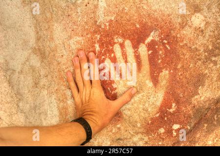 La main d'un homme touche une ancienne main à Cueva de las Manos, dans la province de Santa Cruz, en Argentine Banque D'Images