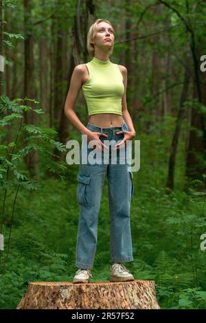 jeune belle femme se tient sur une souche dans un parc naturel, regardant dans la distance Banque D'Images