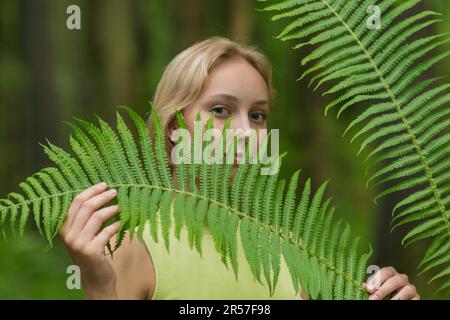 jeune belle femme regardant à travers les feuilles gracieux de fougères dans la forêt Banque D'Images