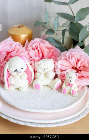 Adorable ours en peluche comestible et petits jouets en chocolat blanc avec des pivoines fraîches et des bougies sur les fonds. Cadeau pour bébé Banque D'Images