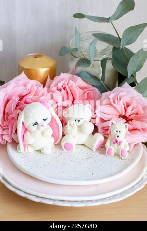 Adorable ours en peluche comestible et petits jouets en chocolat blanc avec des pivoines fraîches et des bougies sur les fonds. Cadeau pour bébé Banque D'Images