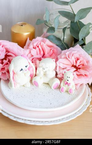 Adorable ours en peluche comestible et petits jouets en chocolat blanc avec des pivoines fraîches et des bougies sur les fonds. Cadeau pour bébé Banque D'Images