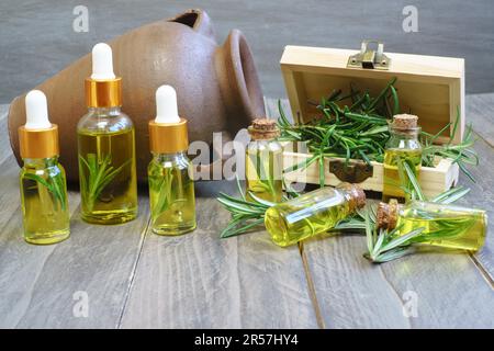 Gros plan d'un compte-gouttes avec une goutte d'huile de romarin à l'arrière-plan plusieurs bouteilles d'essence de romarin dans une boîte en bois Banque D'Images