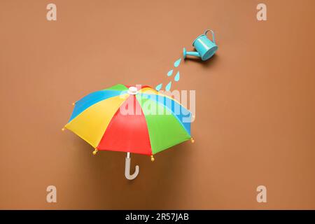 Composition créative avec mini arrosoir et parapluie sur fond marron Banque D'Images