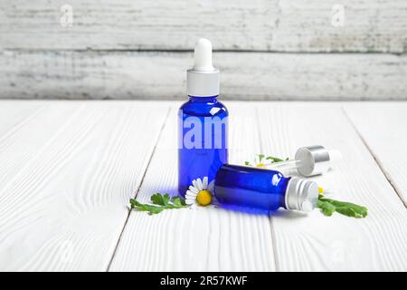 Bouteilles d'huile essentielle et fleurs de camomille sur une table en bois clair Banque D'Images