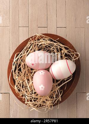 Trois œufs de Pâques roses dans un nid sur une table en bois, concept traditionnel de Pâques Banque D'Images