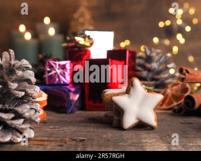 Des étoiles de cannelle empilées sur une table en bois avec des boîtes-cadeaux colorées et des lumières de Noël floues Banque D'Images