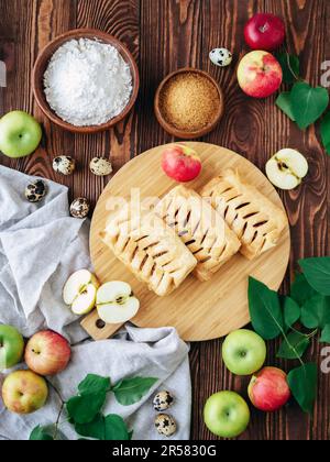 Photographie culinaire vue de dessus. Pâte feuilletée au four bouffée de pomme croustillante avec des ingrédients sur une table en bois rustique. Tartes feuilletées aux pommes, cassonade Banque D'Images