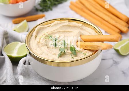 Délicieux houmous avec bâtonnets de grissini servis sur une table en marbre blanc, en gros plan Banque D'Images