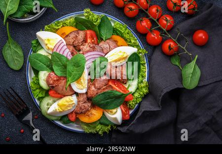 Salade Périgord avec foie de poulet rôti, tomates rouges, concombres, œufs durs, laitue et épinards. Arrière-plan de la table de cuisine noire, vue du dessus Banque D'Images