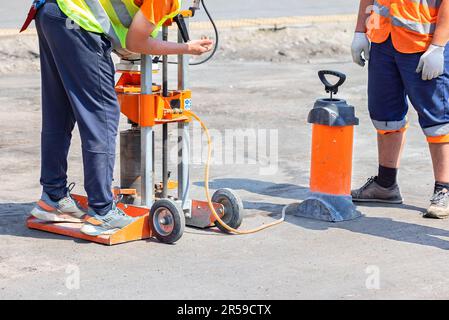 Les constructeurs de routes ont mis en place une machine de forage à essence pour couper des échantillons de béton bitumineux par temps ensoleillé. Banque D'Images